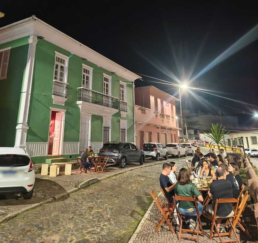 O casarão verde do Paredão Bar à noite, com mesas cheias na rua de pedra do centro histórico de Itabira
